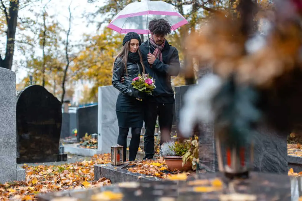Couple mourning a deceased loved one on cemetery in fall standing between the graves