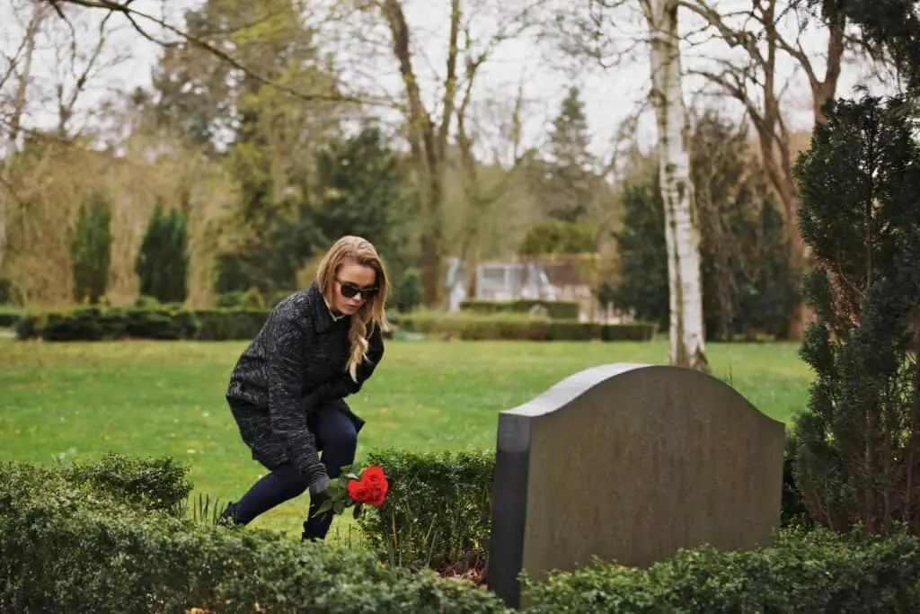 Young woman placing flowers on the grave of a deceased family member at cemetery.