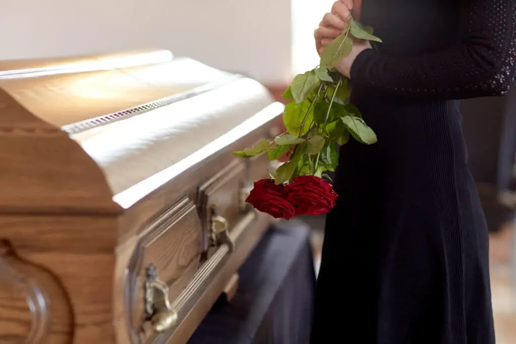 woman with red roses and coffin at funeral